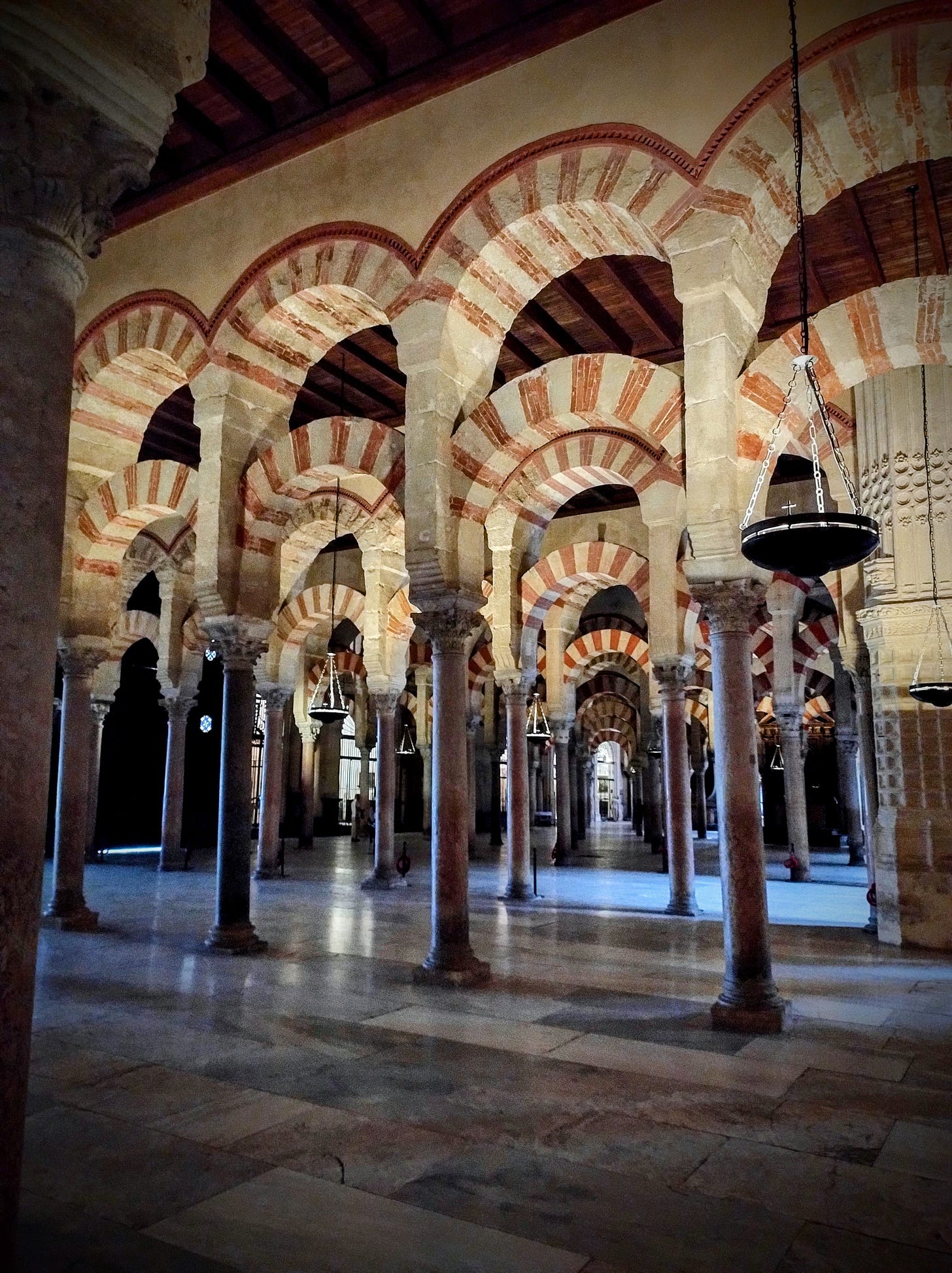 An image showing the Mezquita of Cordoba. There are many repeating arches, with red and white detail as well as a smooth marble floor. 