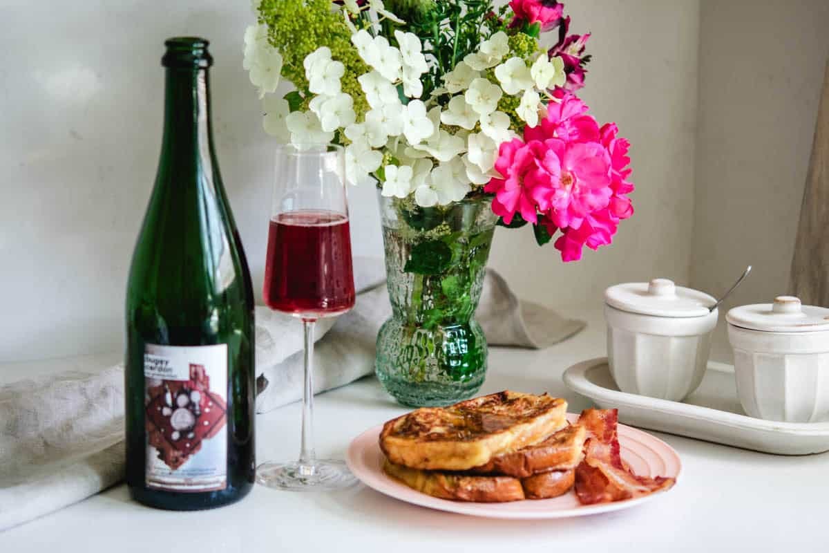 Wine bottle and glass of bugey cerdon with french toast and bacon with flowers in the background Wine bottle and glass of bugey cerdon with french toast and bacon with flowers in the background