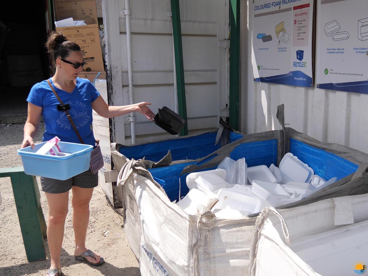 Brunette woman in shorts dropping off her recycling at the local recycling depot.