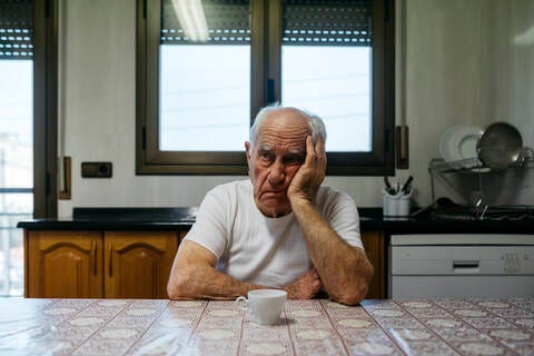 Sad man sitting at table in kitchen stock photo