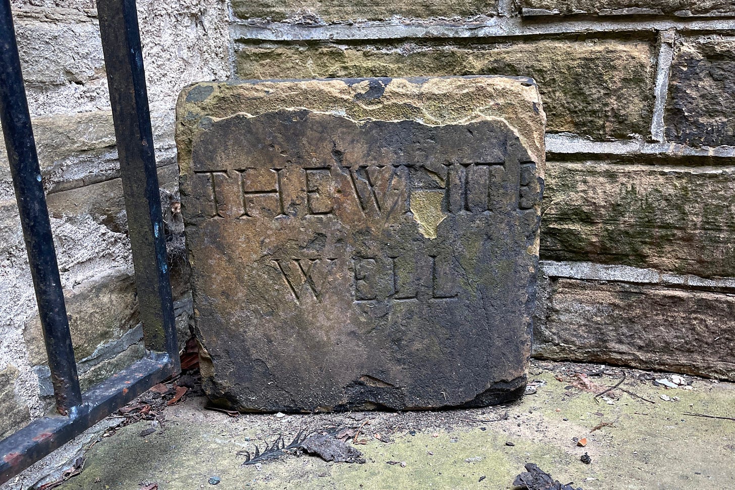 A stone tablet in the corner of two stone walls with the words THE WHITE WELL carved in it..