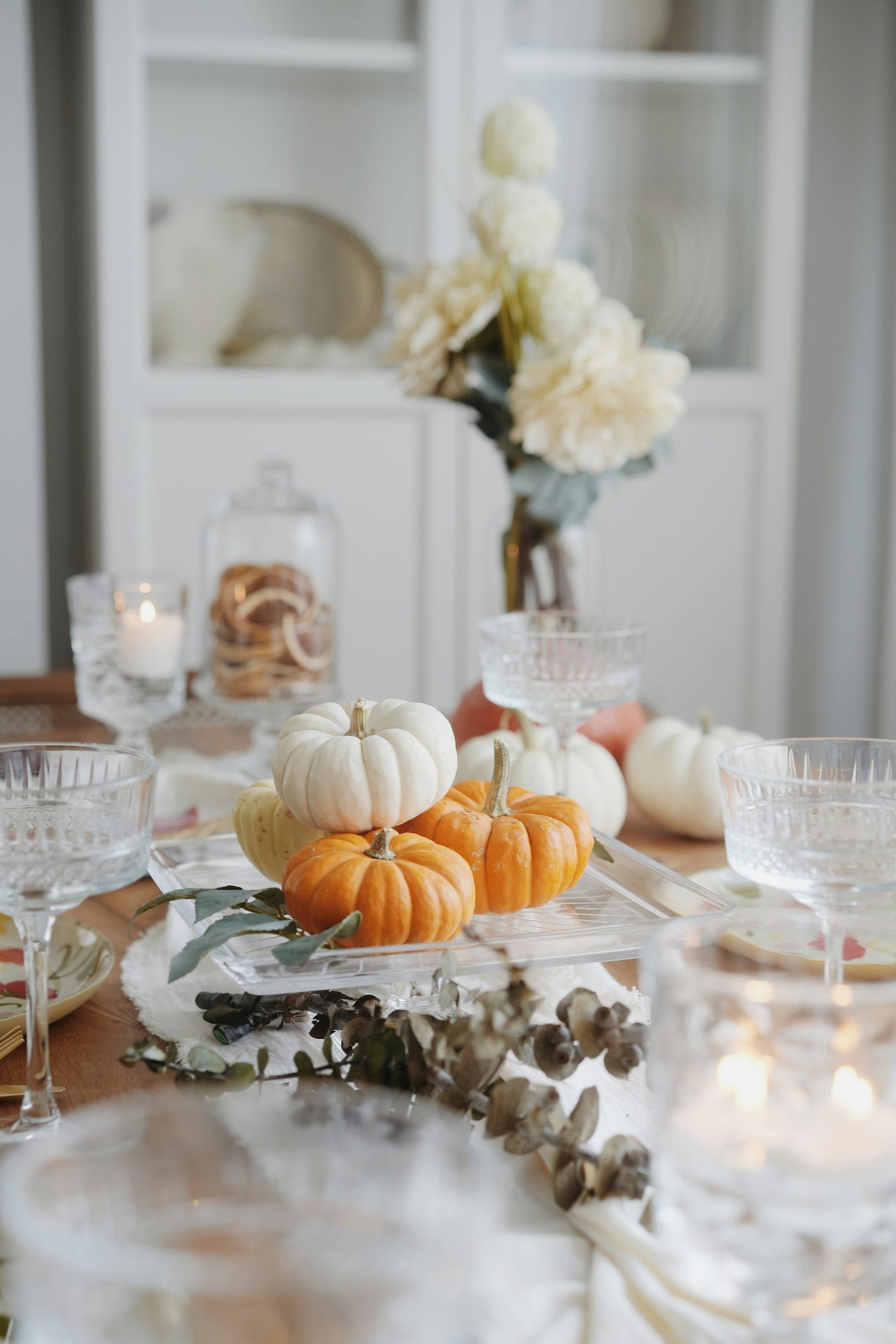 A dining table is set in fall fashion, displaying small pumpkins of different colors, dry branches, small plates and champagne glasses.