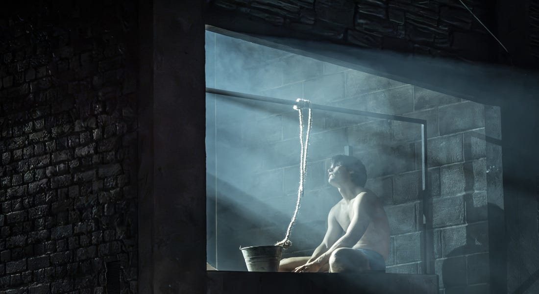 A man sat in a windowsill next to a bucket, with blue light shining on him