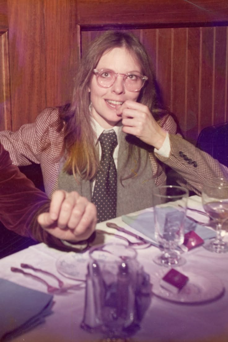 This may contain: two people sitting at a table with wine glasses in front of them and one person holding something up to her mouth