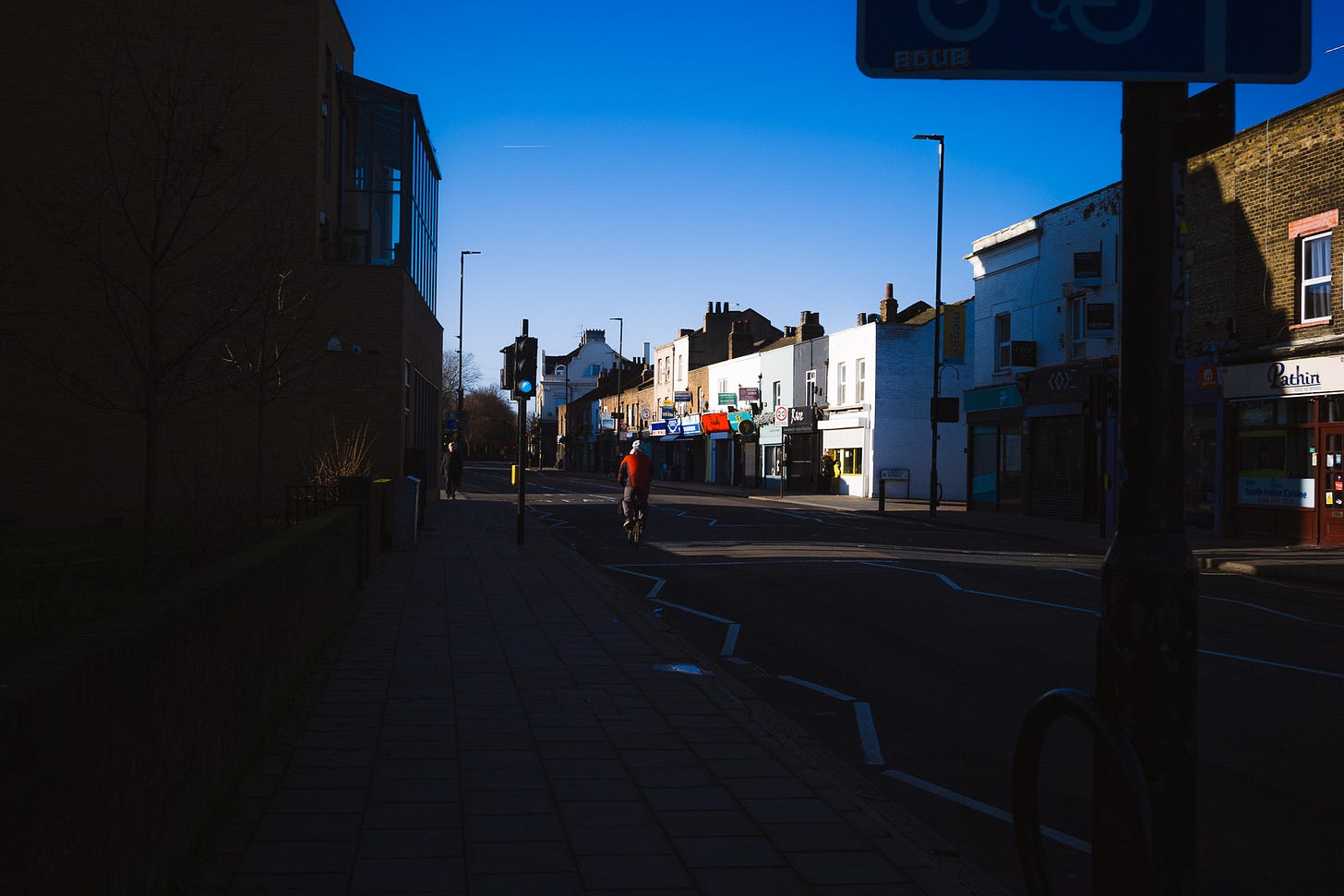 Biker in a red vest is caught in a shaft of sunlight in a street alternating between shadow and sun