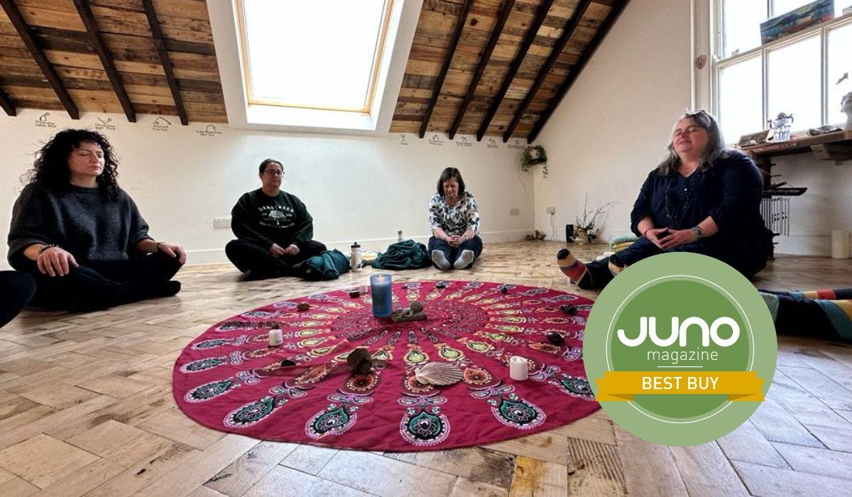A Mama Retreat Day, showing women sat in circle with eyes closed in a bright room. There is a circular mandala throw in the centre with various objects and candles