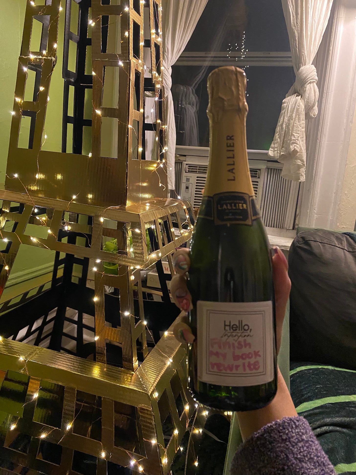 A mini bottle of Lallier champgne being held in front of a cardboard Eiffel Tower that says Finish My Book Rewrite
