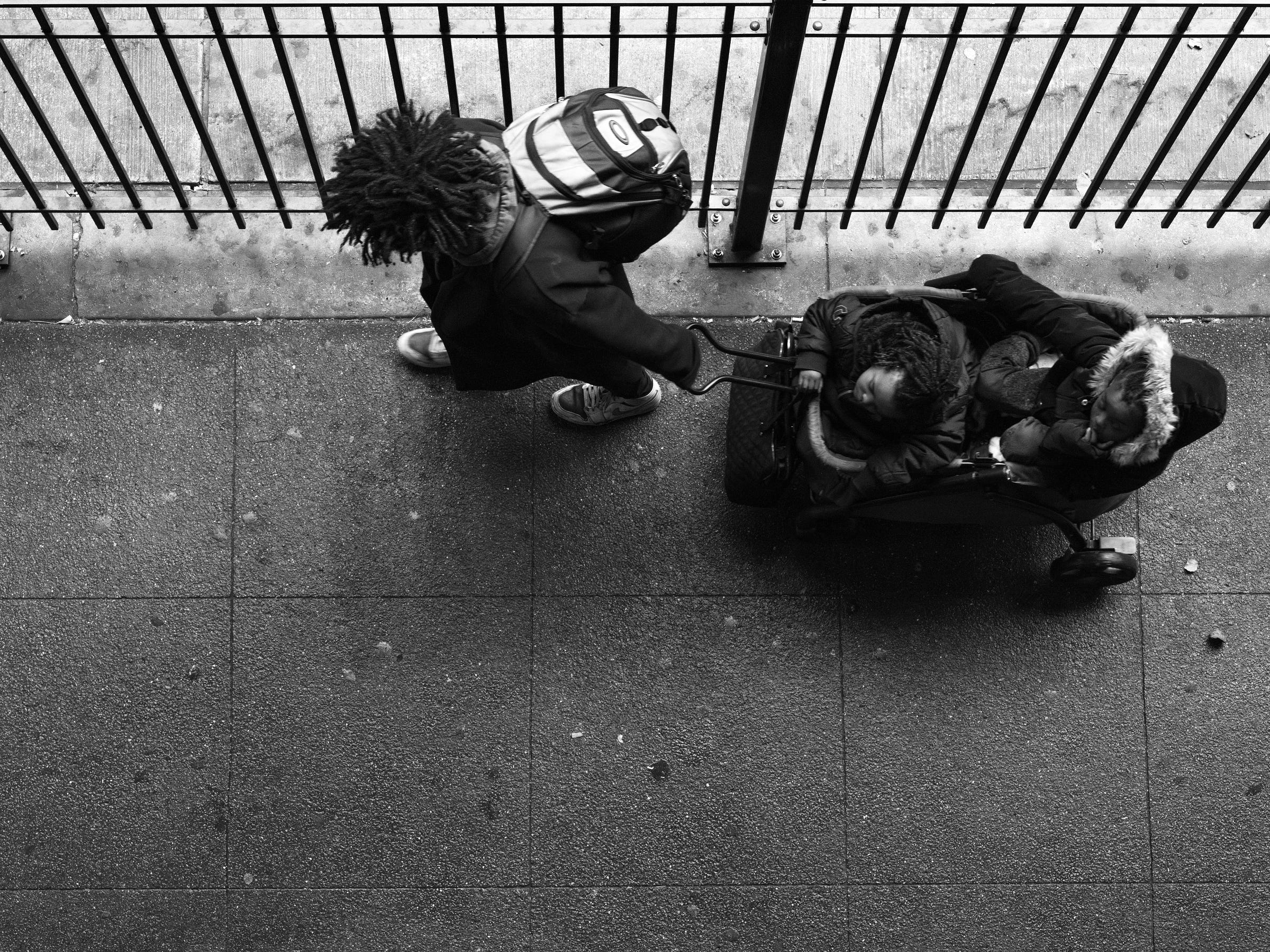 Black-and-white photo with bird's eye view of man pulling two children in a cart.