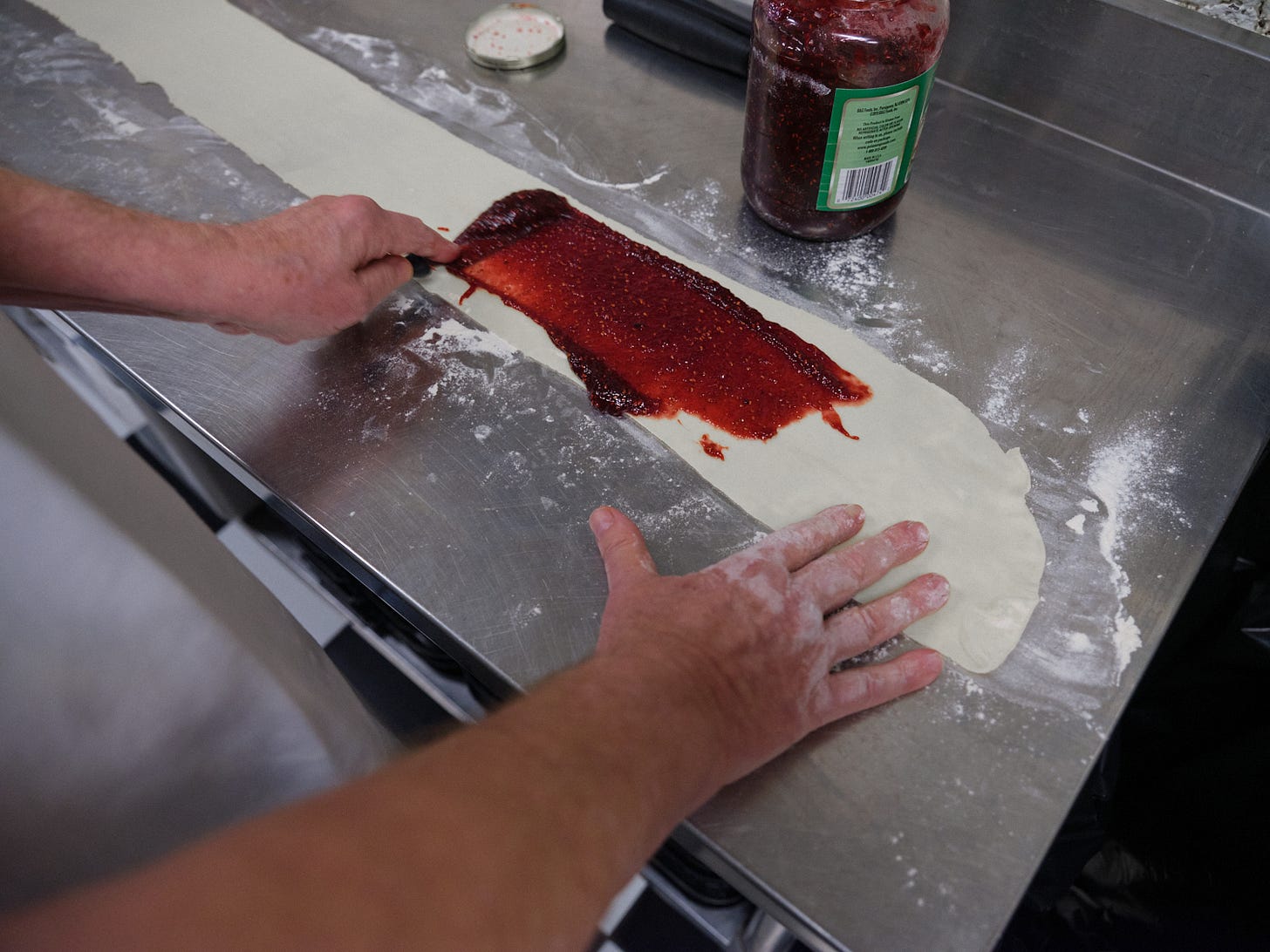 Larry spreads raspberry preserves on top of his sheet of cookie dough