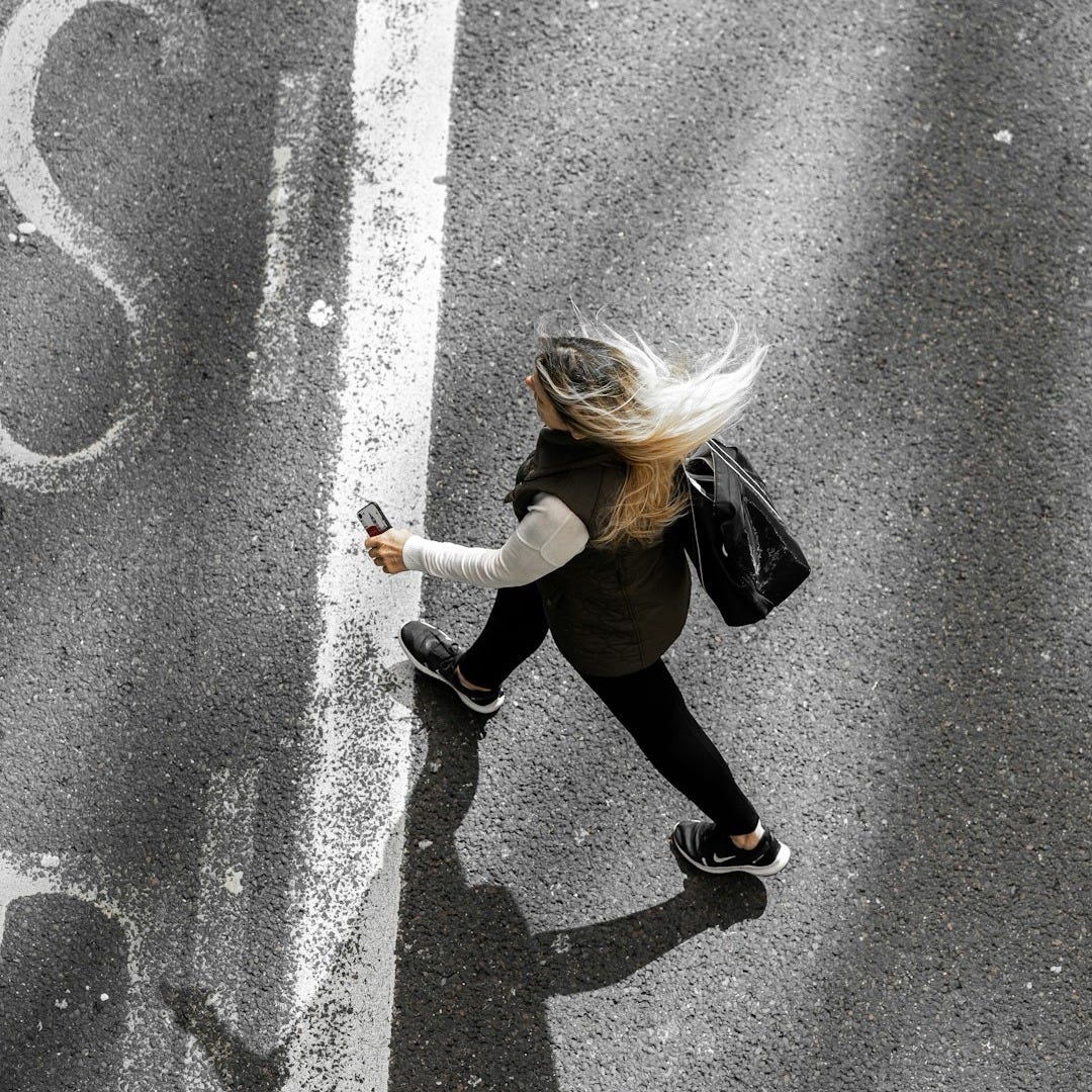 woman in black jacket and black pants walking on gray asphalt road during daytime