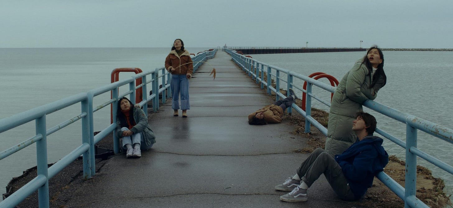 5 young adults hanging out on a concrete pier in winter jackets.