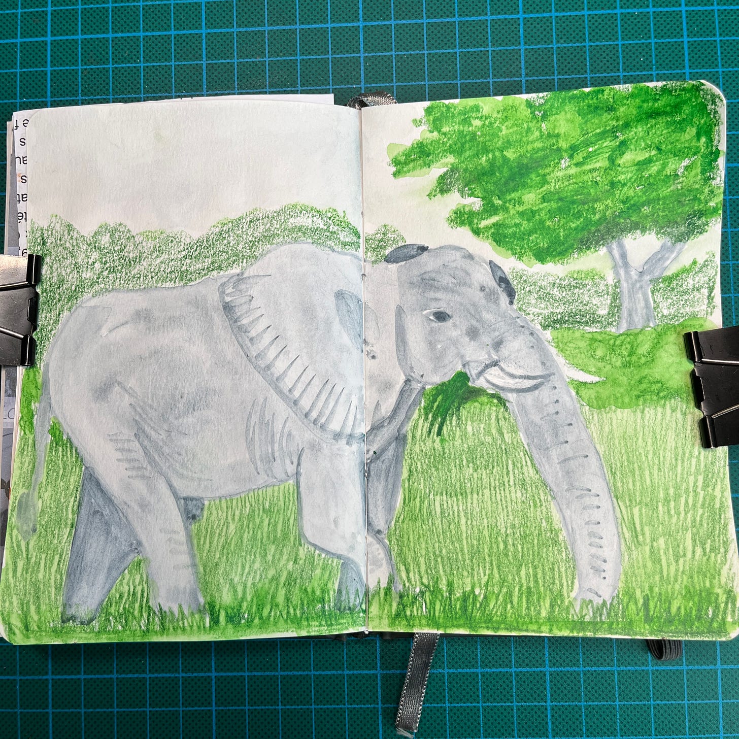 Posé sur mon tapis de découpe, mon sketchbook ouvert sur la double-page où j'ai fait un second dessin le Jour 28 : un éléphant qui mange des herbes. Posé sur mon tapis de découpe, mon sketchbook ouvert sur la double-page où j'ai fait un second dessin le Jour 28 : un éléphant qui mange des herbes.