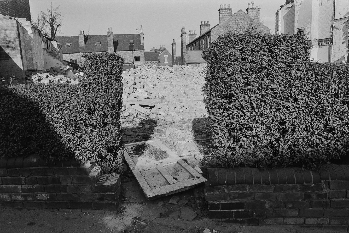 A brick and hedge fence with a pile of rubble and a door behind it A brick and hedge fence with a pile of rubble and a door behind it