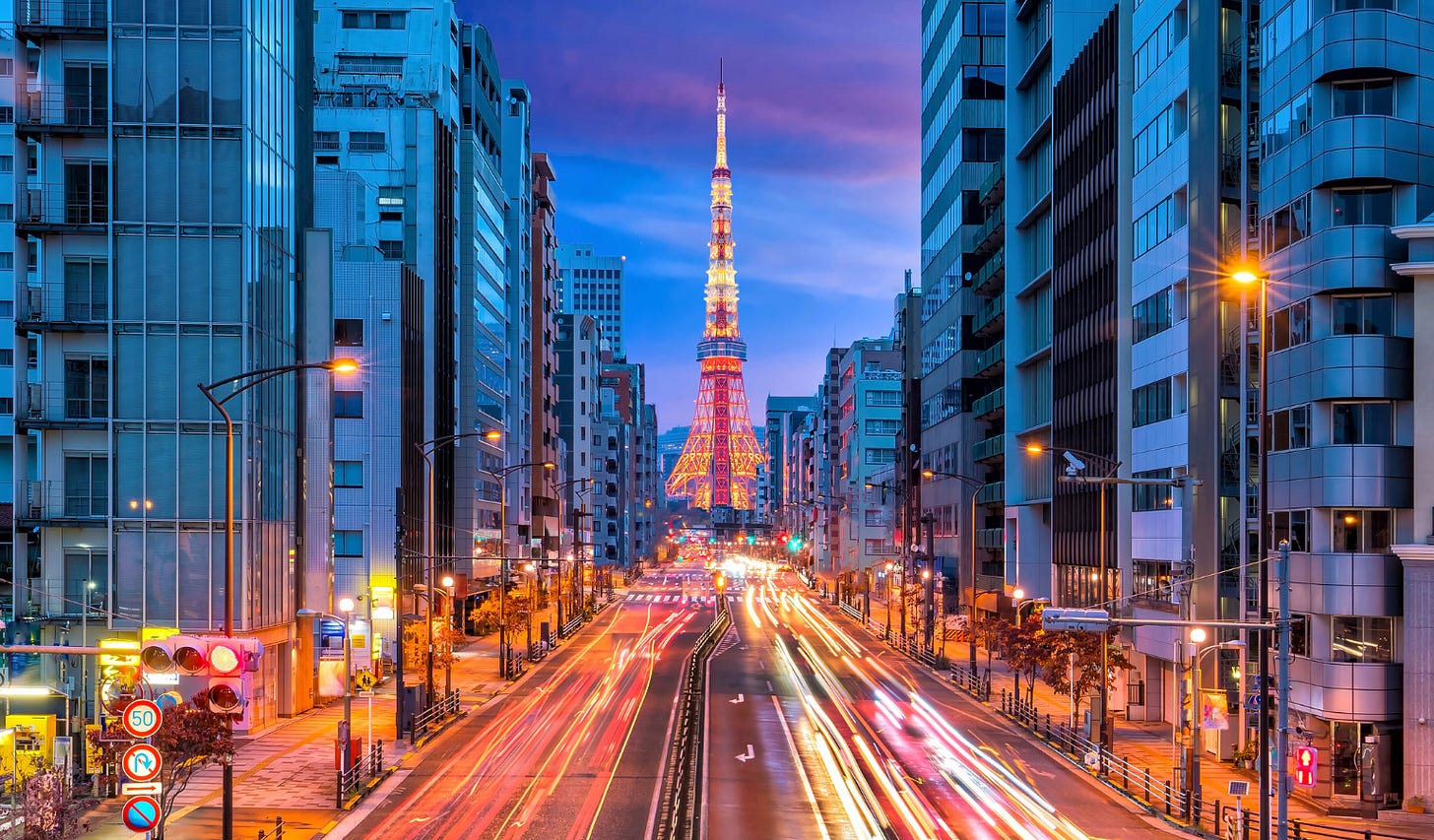 Long-exposure night photo of Tokyo Tower lit up in red and white, viewed down a busy street lined with high-rise buildings, with light trails from passing traffic and a purple twilight sky above. Long-exposure night photo of Tokyo Tower lit up in red and white, viewed down a busy street lined with high-rise buildings, with light trails from passing traffic and a purple twilight sky above.