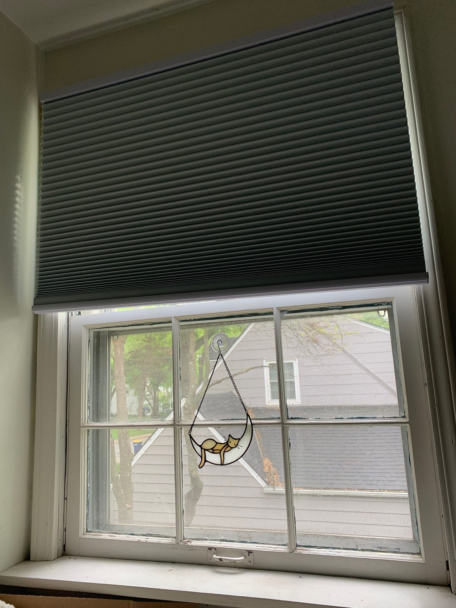 Window with shade halfway up, ornament with a cat sleeping on a half moon