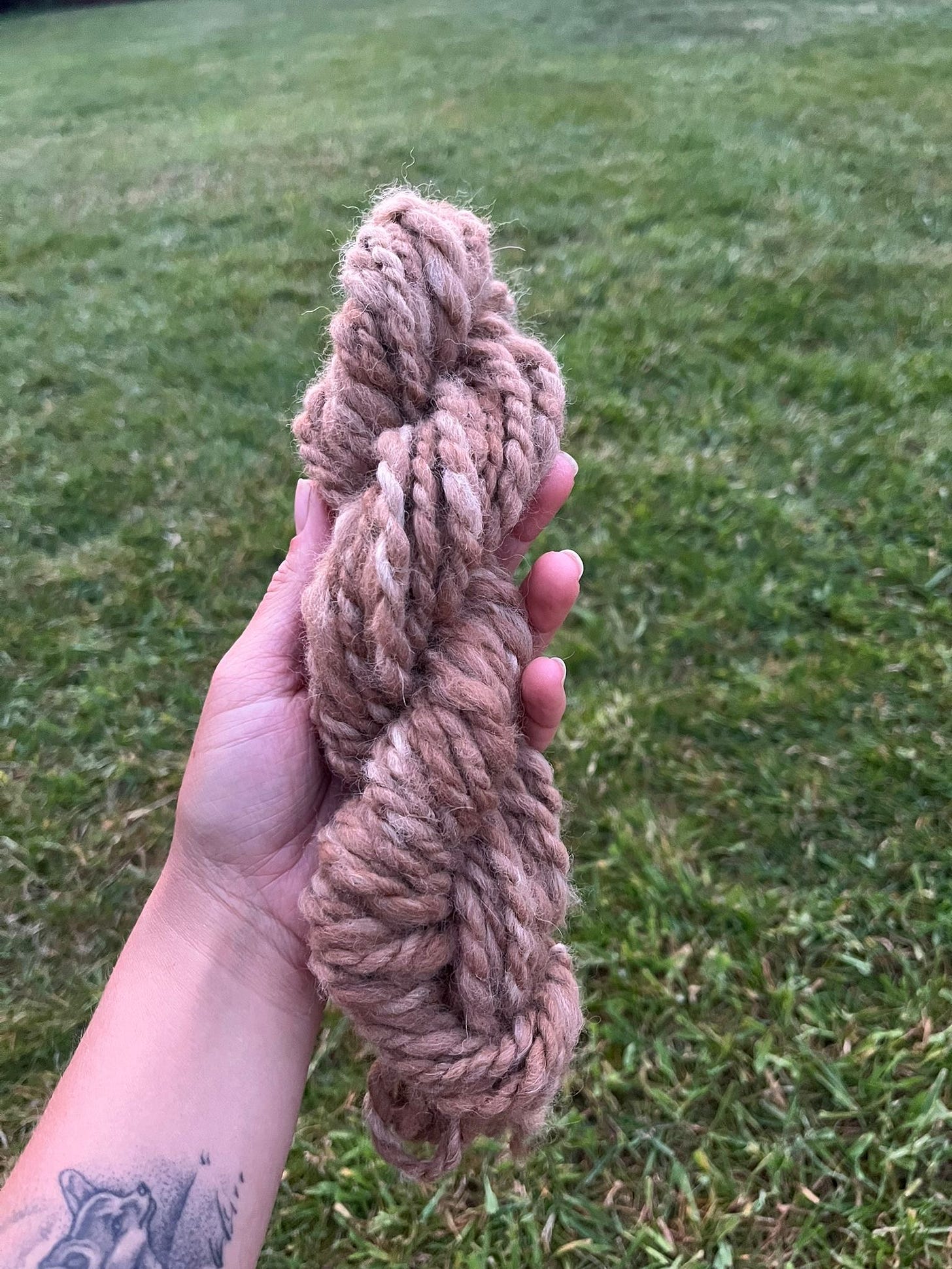 hand spun skein of yarn being held against a background of grass.