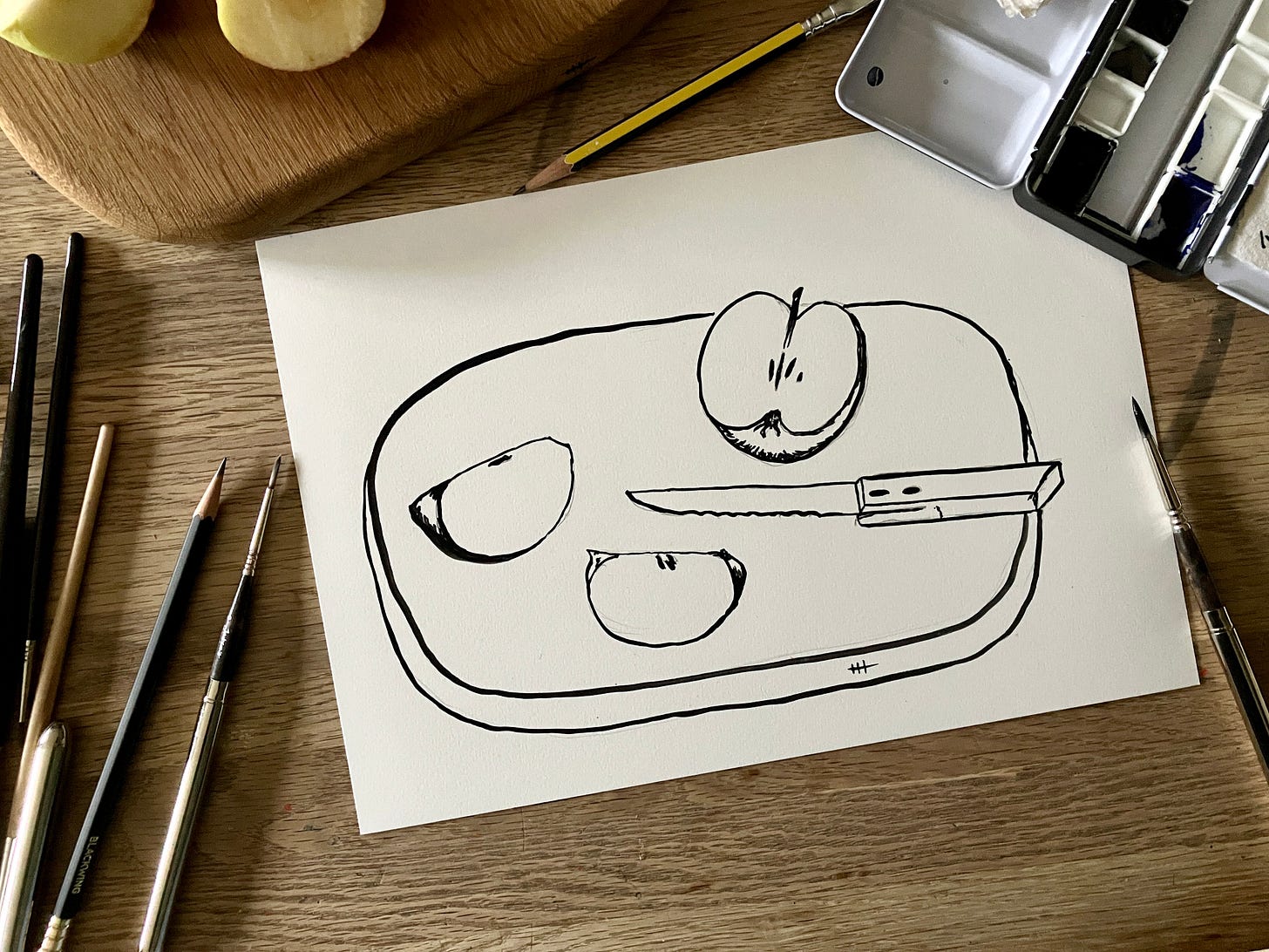 Simple painting of quartered apples sits atop a table surrounded by painting materials
