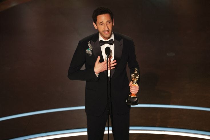 This may contain: a man in a tuxedo holding an award and making a speech on stage