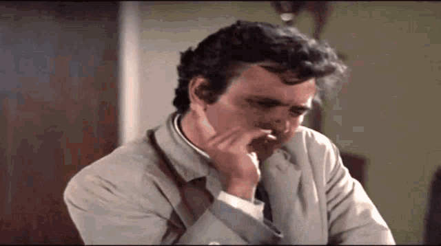 a man in a suit and tie is smoking a cigarette while sitting at a table .