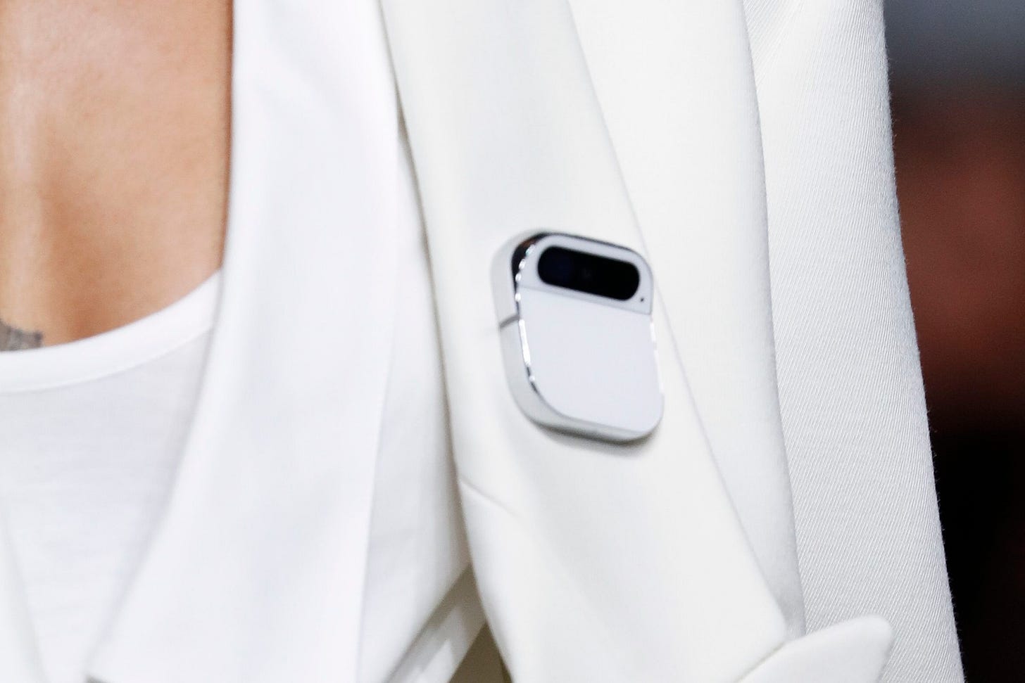 Close-up shot of a white Ai Pin on a grayish white jacket lapel.