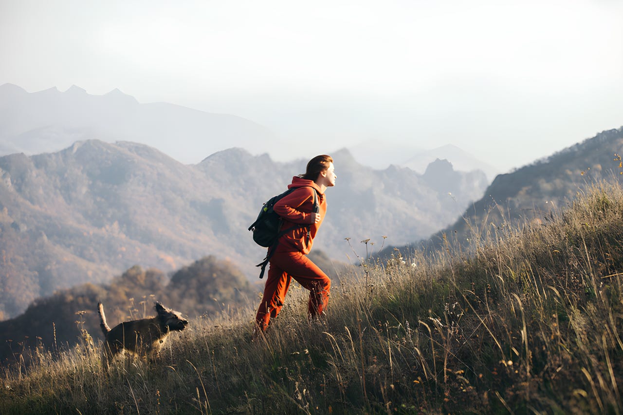 Woman hiking up grassy hill with her dog.