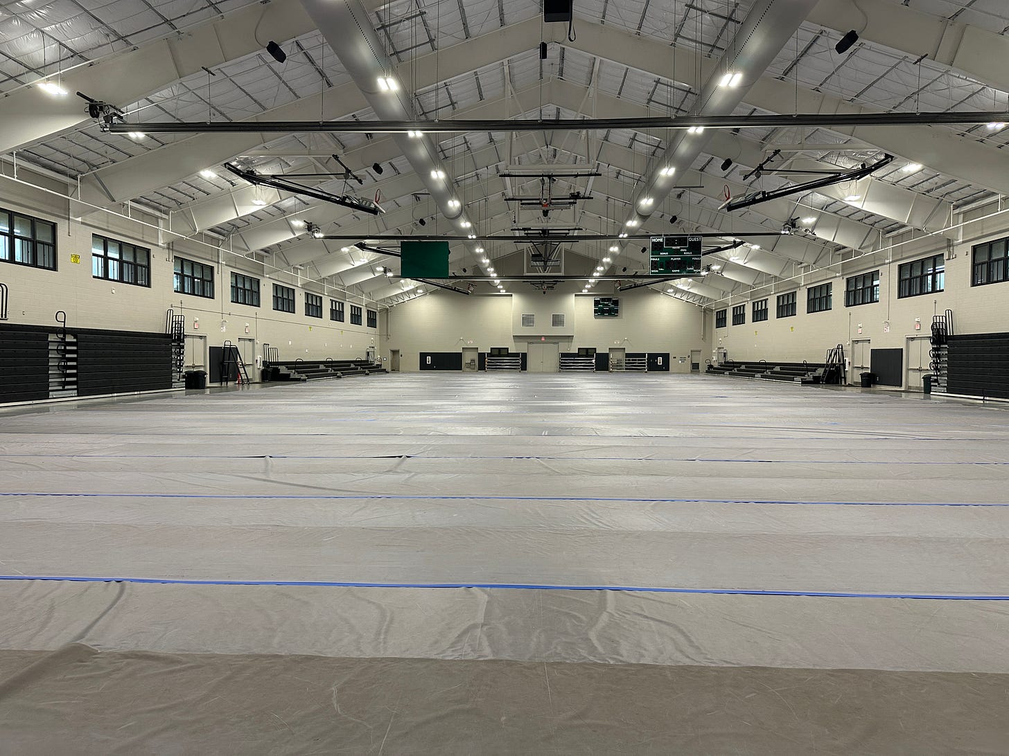 a large empty community gym with bleacherd and basketball hoops in the distance.