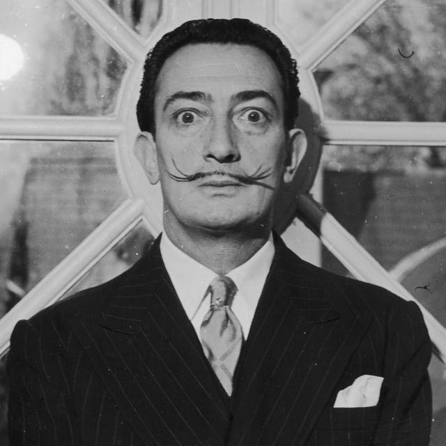 salvador dali stares wide eyed into the camera, he has his signature thin mustache and wears a suit with a pocket square