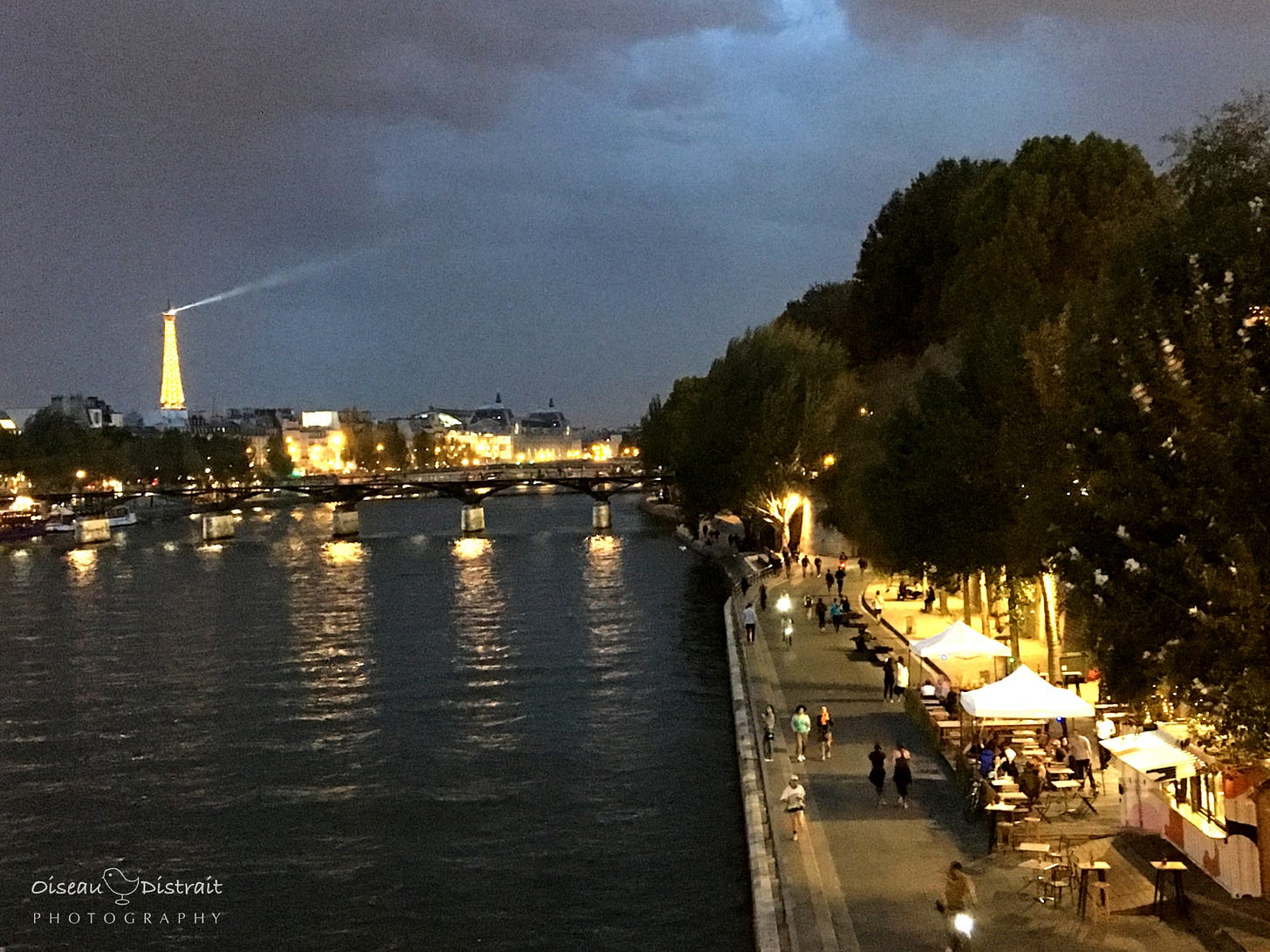 A grey cloudy sky with lighting of the Eiffel Tower & riverbank along the Seine before raining. A grey cloudy sky with lighting of the Eiffel Tower & riverbank along the Seine before raining.