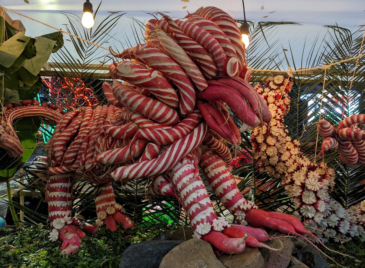 A lion with a striped red and white mane and white eyes is roughly carved out of red and white radishes. 