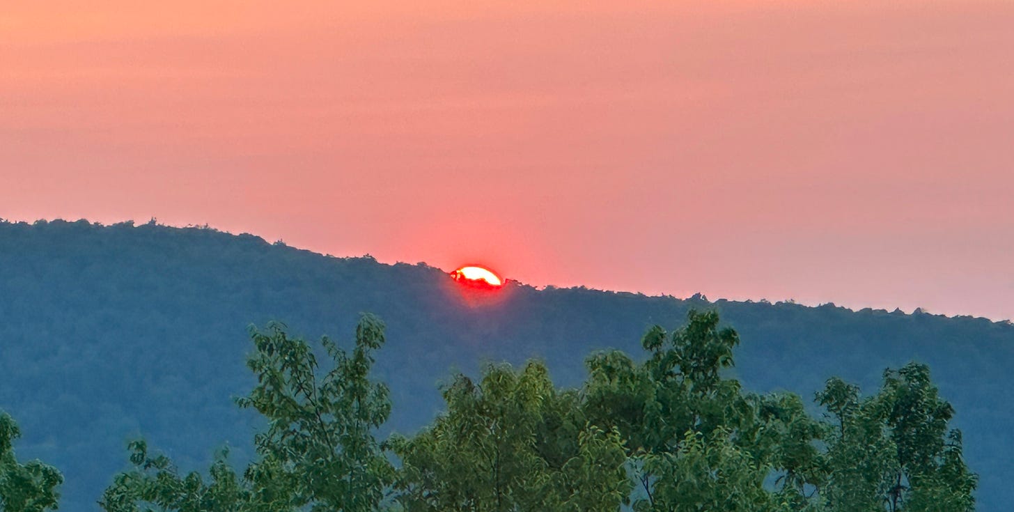 The sun sets on a distant forested ridge.
