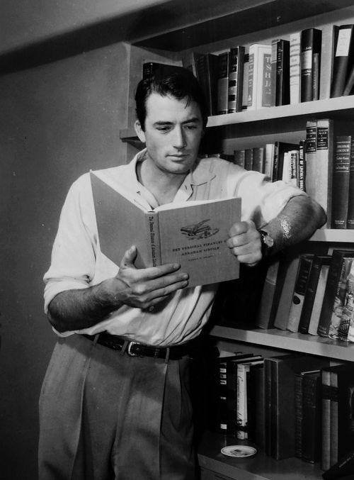 This may contain: a man standing in front of a bookshelf holding a book