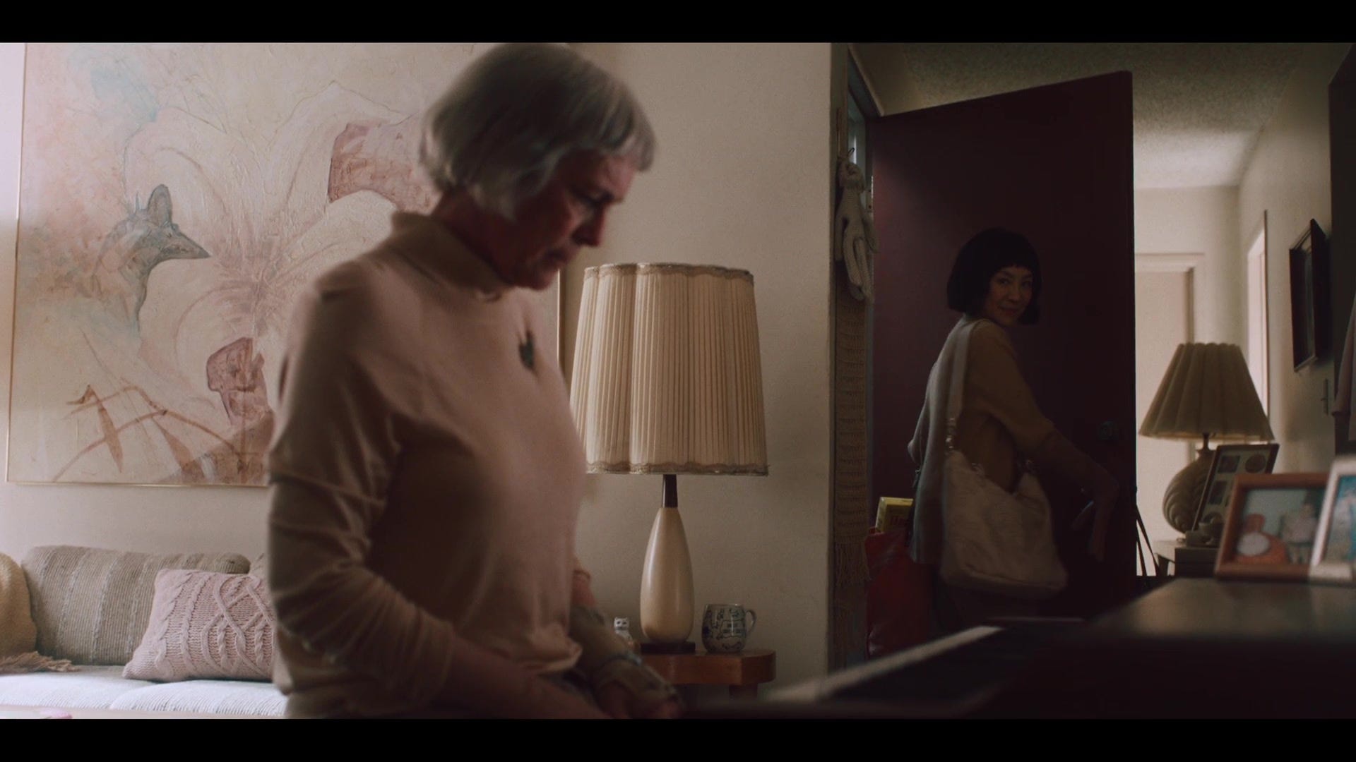 Screenshot from an alternate universe from "Everything Everywhere All At Once." Deirdre sits sadly at the piano, Evelyn comes in with a smile.