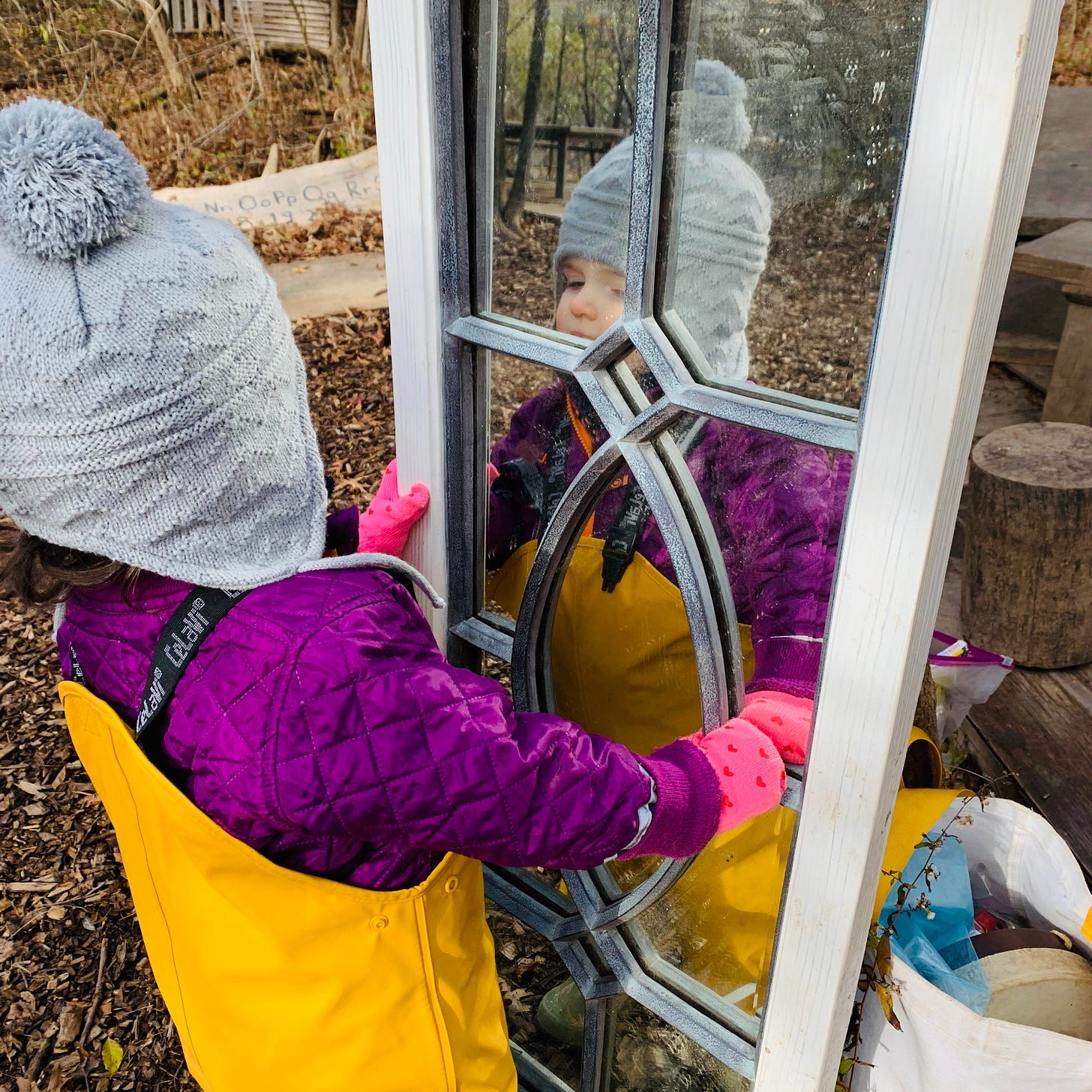 A small child looks into a mirror in an outdoors area