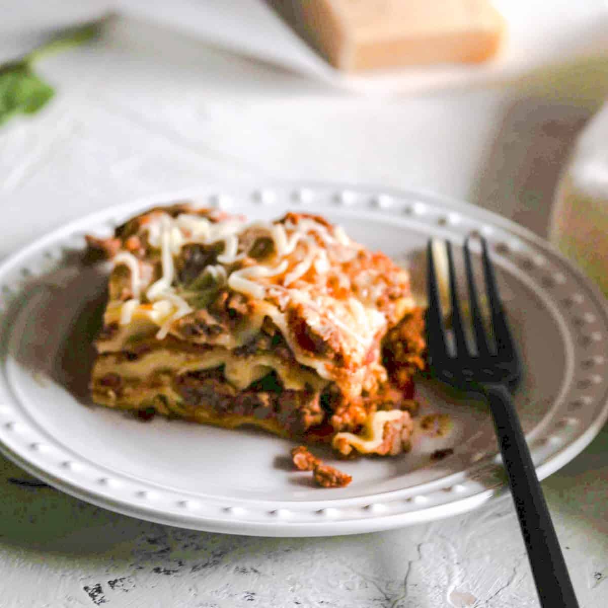 Homemade lasagna on white plate with black fork.