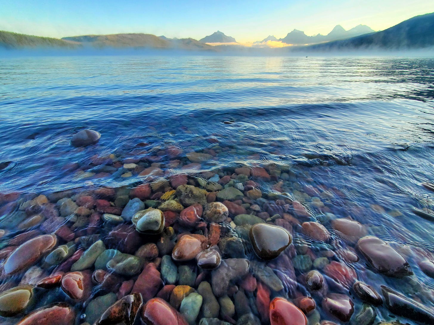 Colorful rocks on a shore, fog, mountains in the background