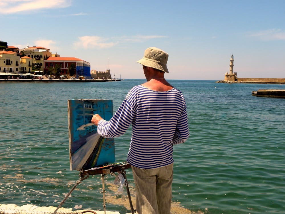 Free A painter capturing the scenic view of Chania lighthouse by the sea, Greece. Stock Photo