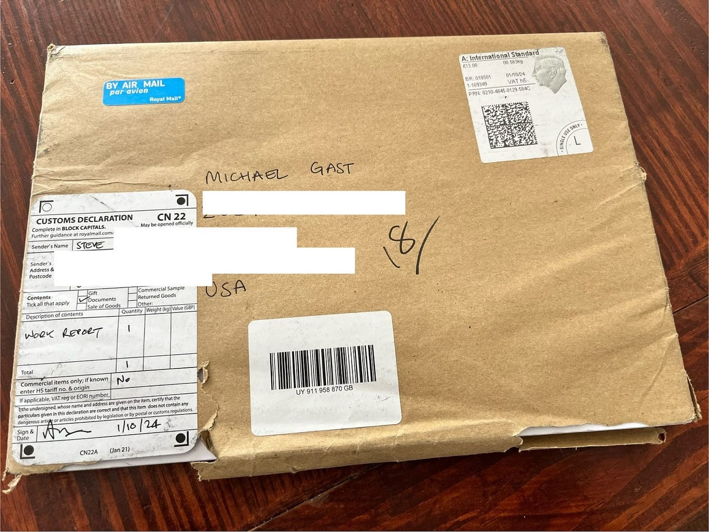 a brown manila envelope, ragged at the edges, with a blue "by air mail" stamp in the top left corner, a customs declaration form on the bottom left corner and Michael's name and address in the middle. There is a stamp with the face of King Charles in profile on the top right.