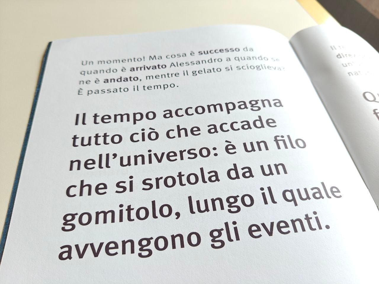 Una pagina aperta del libro "Tempo" di Piero Martin, illustrato da Fabio Magnasciutti. Si intravede la pagina di sinistra con un breve testo in alto: "Un momento! Ma cosa è successo da quando è arrivato Alessandro a quando se ne è andato, mentre il gelato si scioglieva? È passato il tempo.". Sulla stessa pagina, poco sotto e al centro, si trova una citazione in caratteri grandi e neri: "Il tempo accompagna tutto ciò che accade nell'universo: è un un filo che si srotola da un gomitolo, lungo il quale avvengono gli eventi.". Il libro è aperto su una superficie chiara, con un'ombra morbida che suggerisce una fonte di luce laterale.