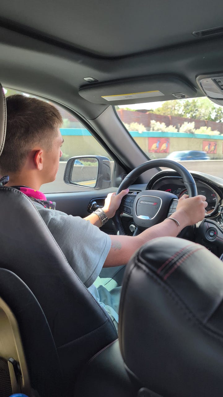 Two images: One of the author (Rosa Linda Román) in the backseat of her Dodge Durango with New Mexico mountains in the background and a laptop on her lap. The other of her son driving in the front seat.