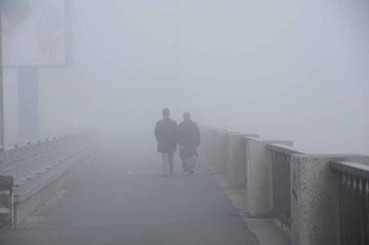 A couple crossing a misty fog covered bridge, hand in hand.