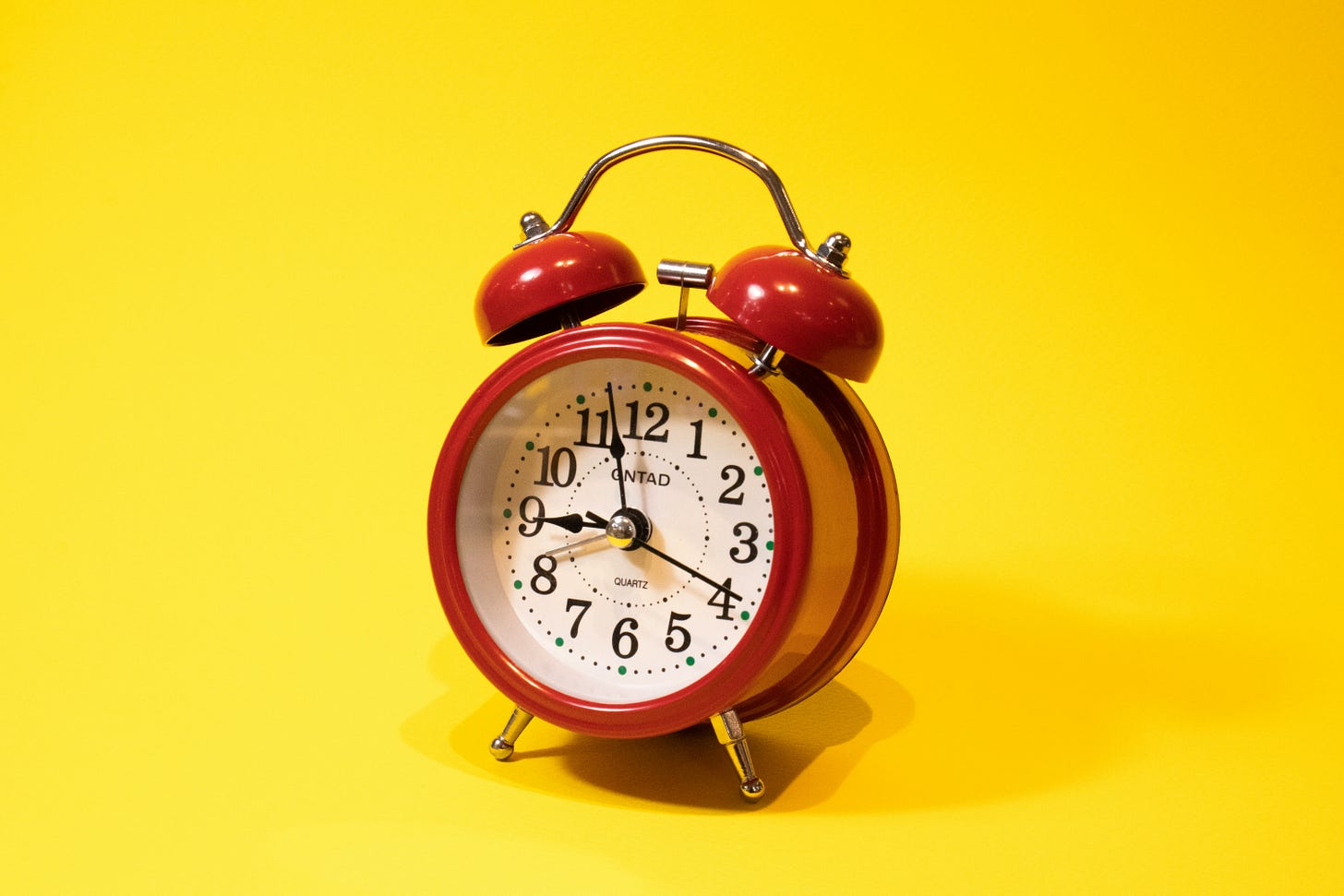Red and white alarm clock on yellow background.