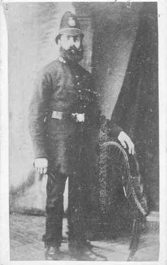 A police officer in uniform standing with a hand on a chair. 