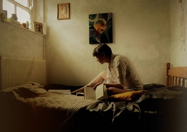 This may contain: a person sitting on a bed with a book in their hand and looking at it