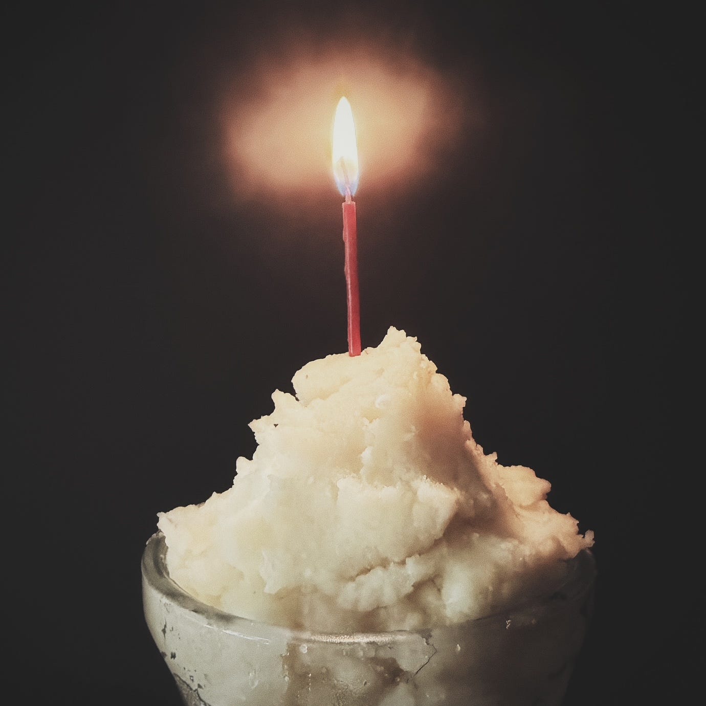 A sundae glass filled with mashed potatoes with a lit red candle sticking out of the top. A sundae glass filled with mashed potatoes with a lit red candle sticking out of the top.