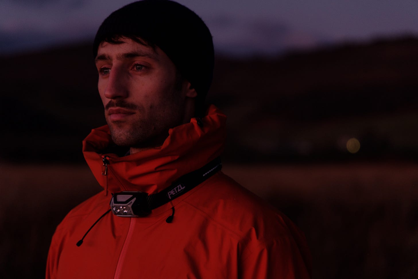A person stands facing a distant hill in the soft blue hour of dawn. The first light hasn’t yet touched the landscape, and everything is still. The figure appears contemplative, silhouetted gently against the sky, waiting for sunrise.