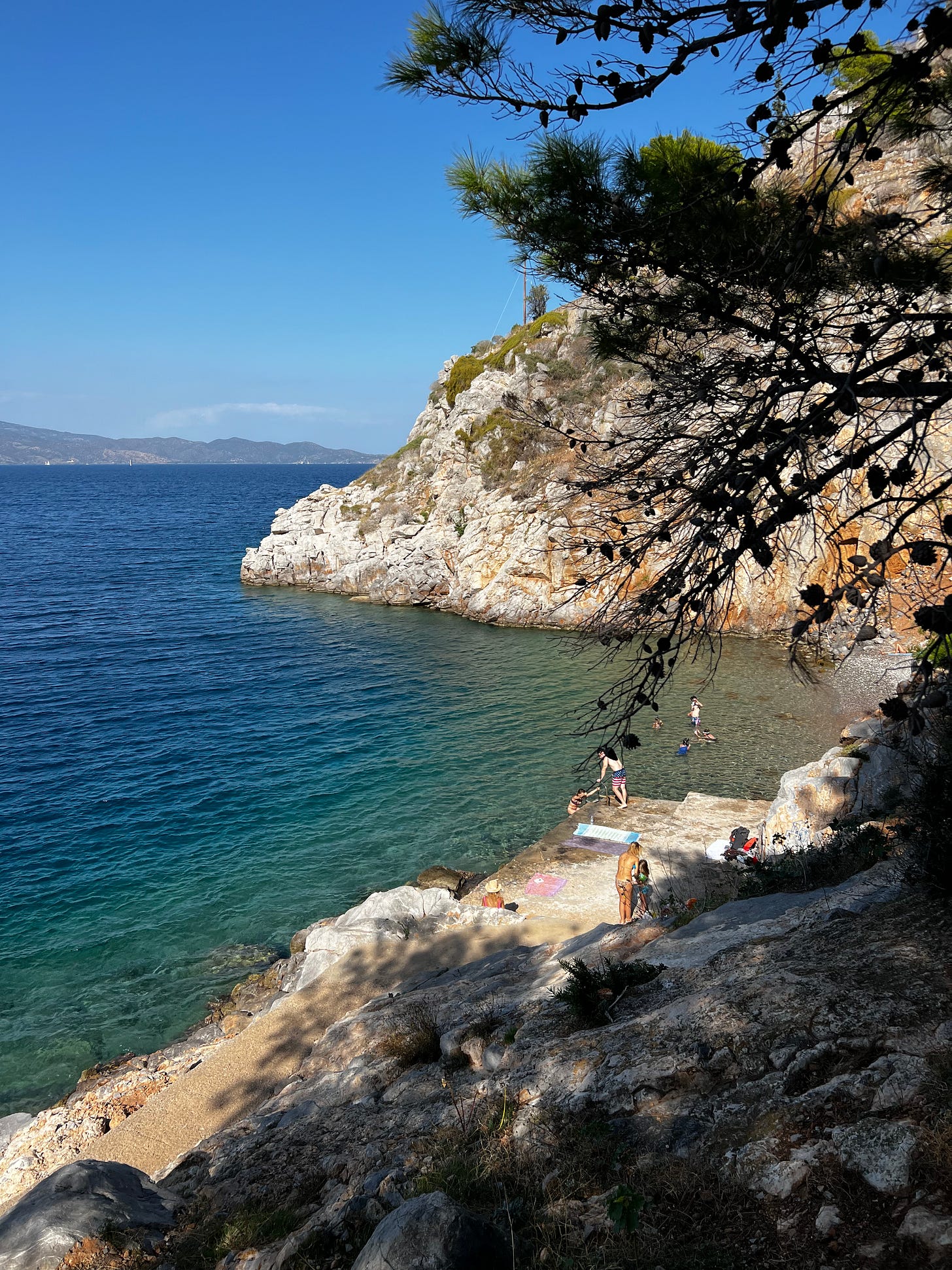 A view from a walking path of a secluded beach, hidden among the rocky cliffside of Hydra, Greece. A few people are enjoying the sea and the sun. A view from a walking path of a secluded beach, hidden among the rocky cliffside of Hydra, Greece. A few people are enjoying the sea and the sun.