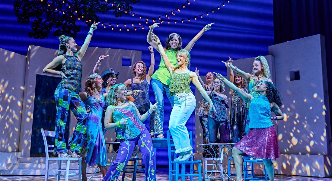 A group of people dancing on stage wearing colourful outfits A group of people dancing on stage wearing colourful outfits