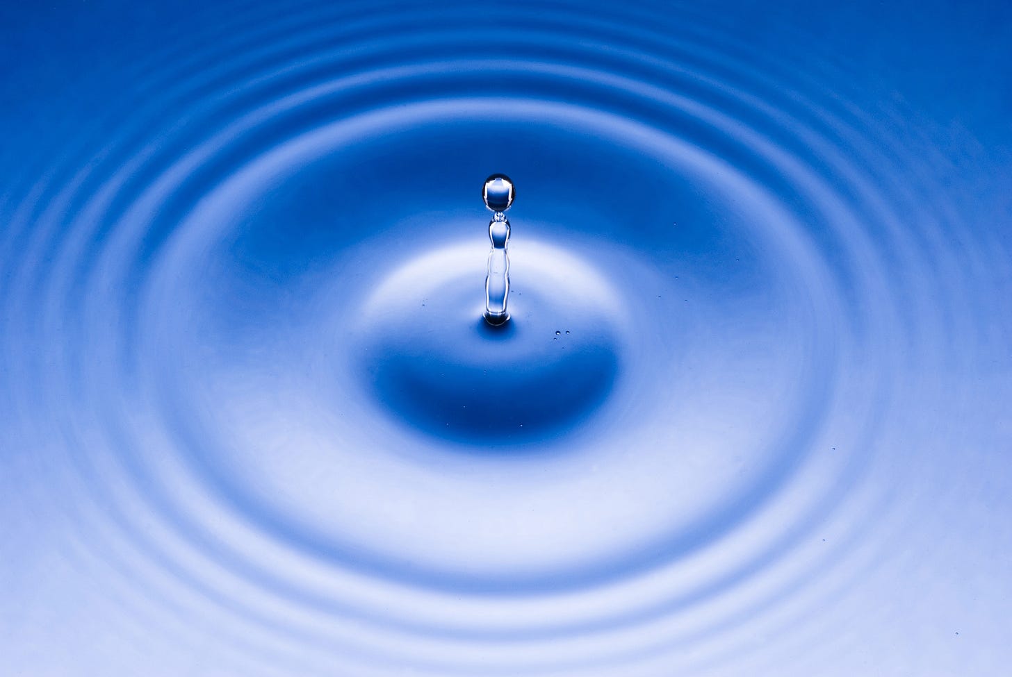 Zoom de uma gota caindo em uma água azulada e formando círculos concêntricos