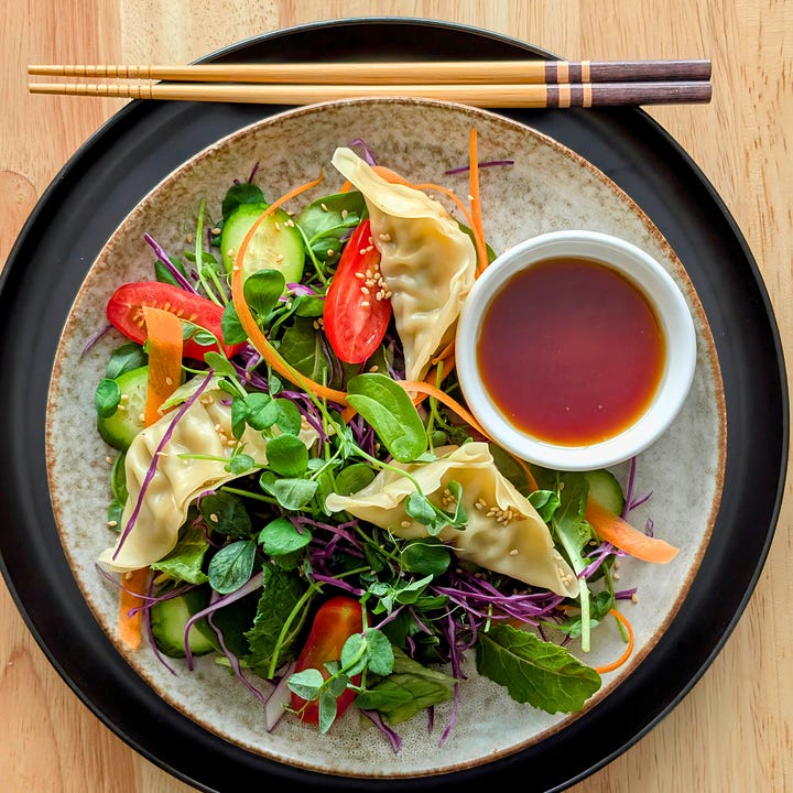 a vibrant dumpling salad served with a small dish of ponzu dipping sauce.