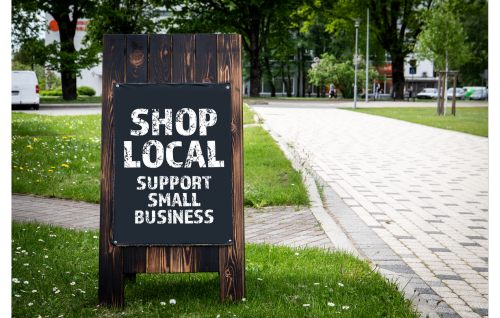 Wooden sign next to a sidewalk. Sign reads "Shop Local support small business"